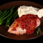 A serving of cranberry chicken on a plate with green beans and mashed cauliflower.