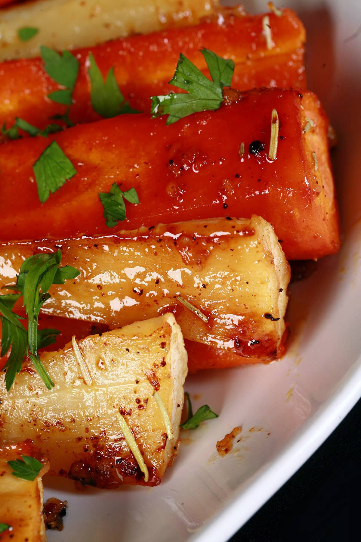 A platter of honey roasted parsnips and carrots, sprinkled with parsley.