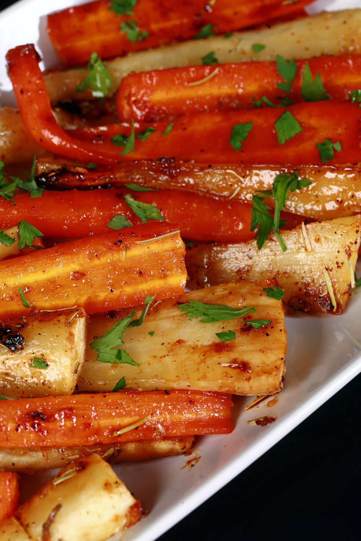 A platter of honey roasted parsnips and carrots, sprinkled with parsley.