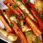 A platter of honey roasted carrots and parsnips, sprinkled with parsley.