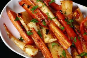 A platter of honey roasted carrots and parsnips, sprinkled with parsley.