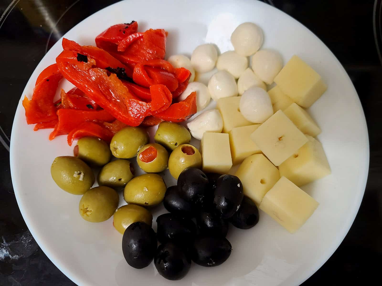 A bowl of drained olives, roasted red peppers, and cheeses.