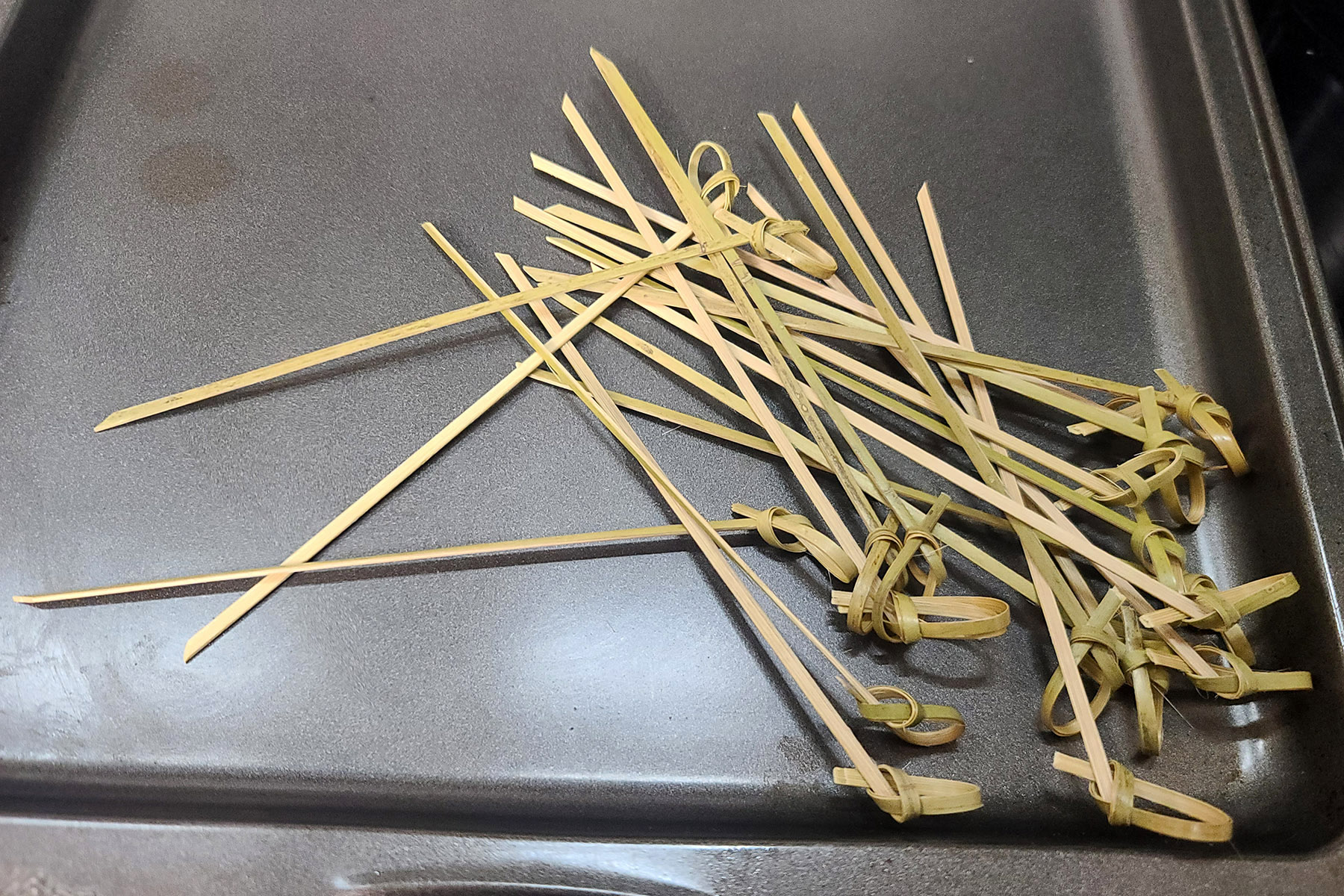 A small pile of bamboo skewers on a pan.
