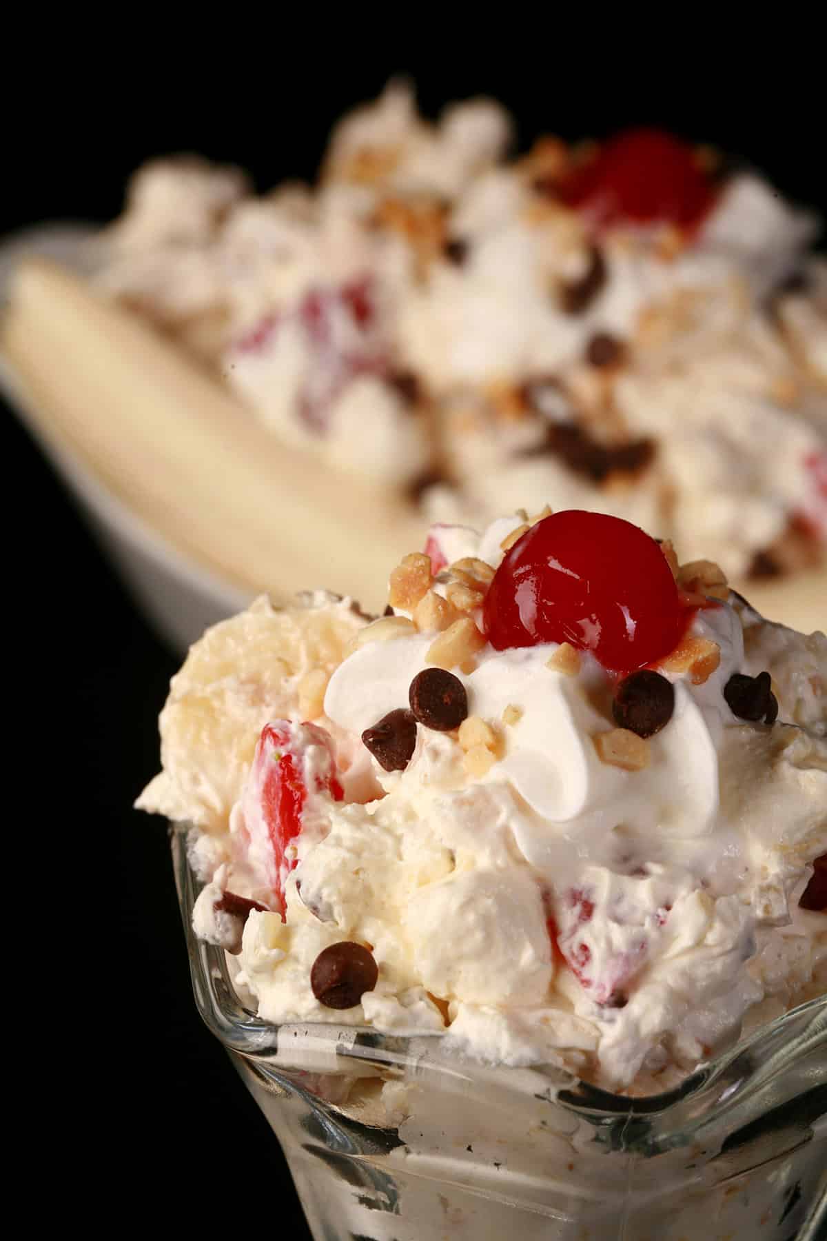 Banana Split Fluff Salad in a glass bowl, in front of a serving done up like an actual banana split.