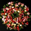 A wreath shaped charcuterie board, made up of antipasto skewers featuring various meats, cheeses, and olives.