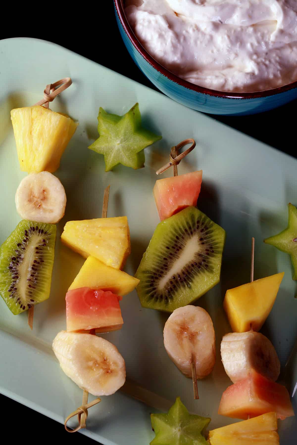 A plate of mixed fruit tropical skewers and a bowl of pina colada dip.