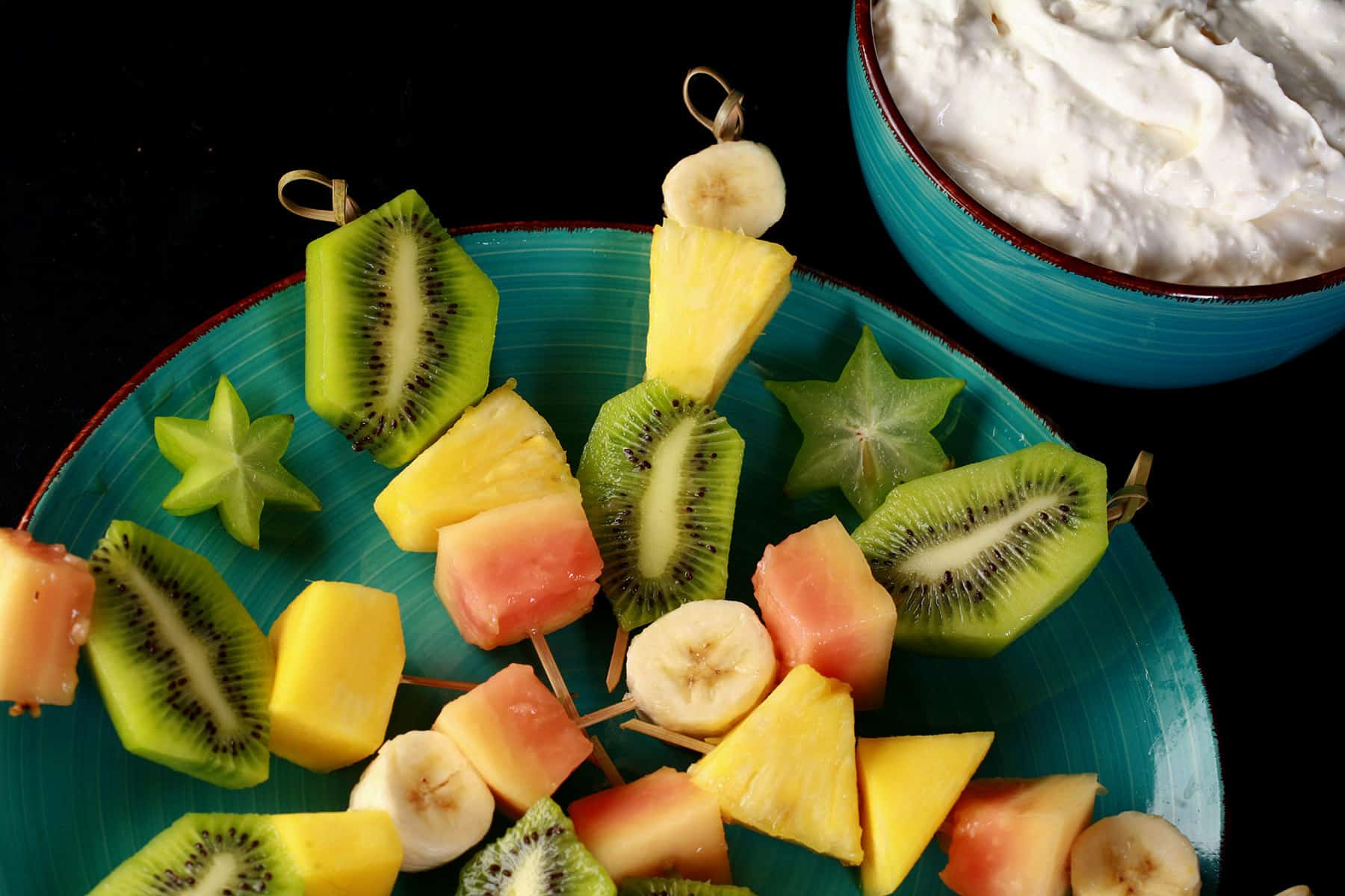 A plate of tropical fruit skewers and a bowl of pina colada cheesecake dip.