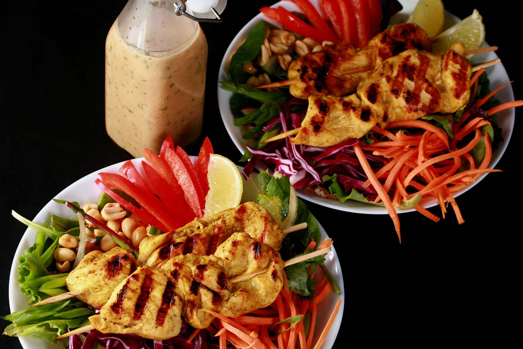 Two grilled chicken satay salads with a bottle of peanut dressing.