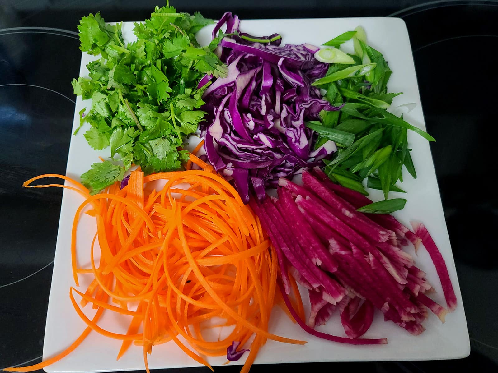 A plate of watermelon radish slices, julienned carrots, sliced purple cabbage, green onions, and cilantro.