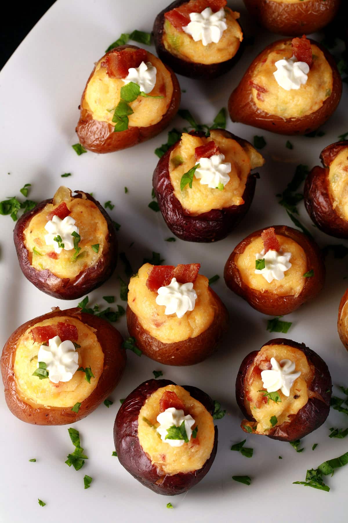 A party platter of loaded mini baked potatoes, topped with sour cream, bacon, and green onion.