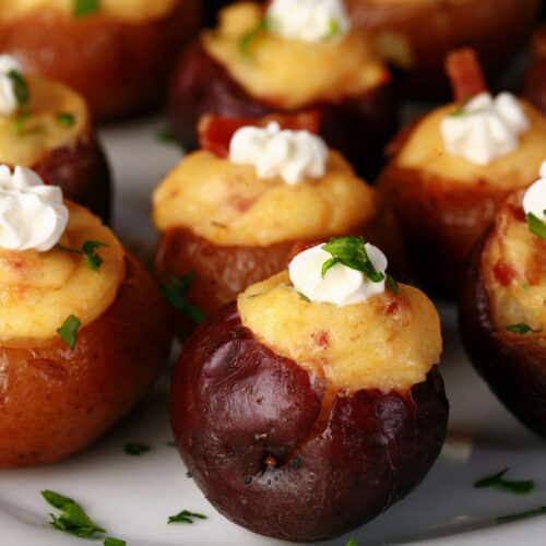 A party platter of mini loaded baked potatoes, topped with sour cream, bacon, and green onion.