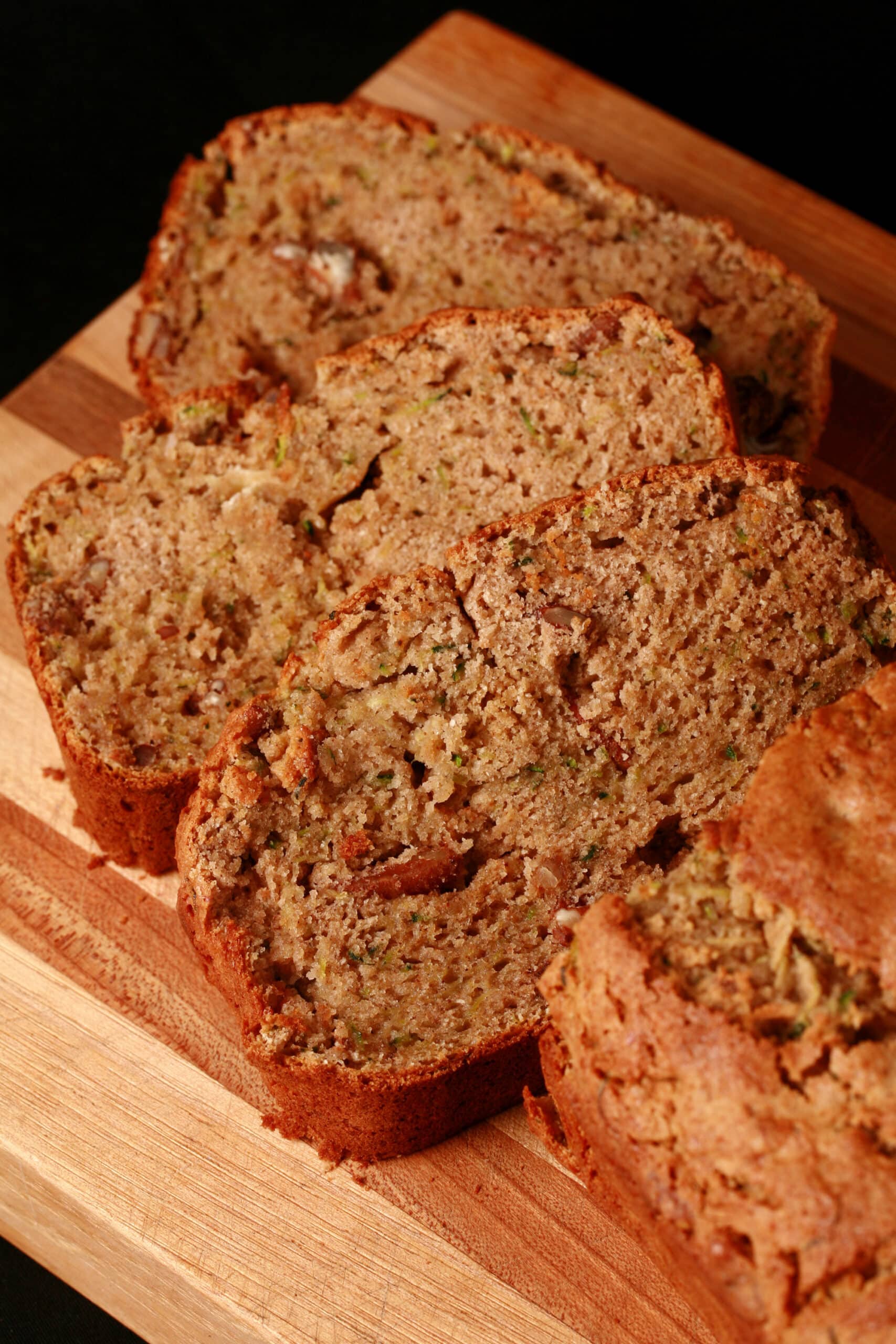 A sliced loaf of gluten free zucchini bread on a wooden cutting board.