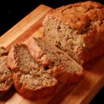 A sliced loaf of gluten free zucchini bread on a wooden cutting board.