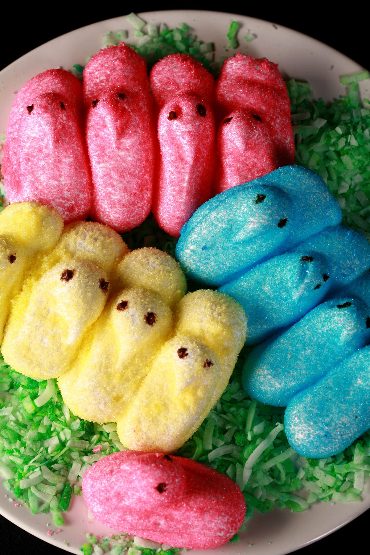 Pink, yellow, and blue chick shaped homemade peeps on a bed of green coconut.