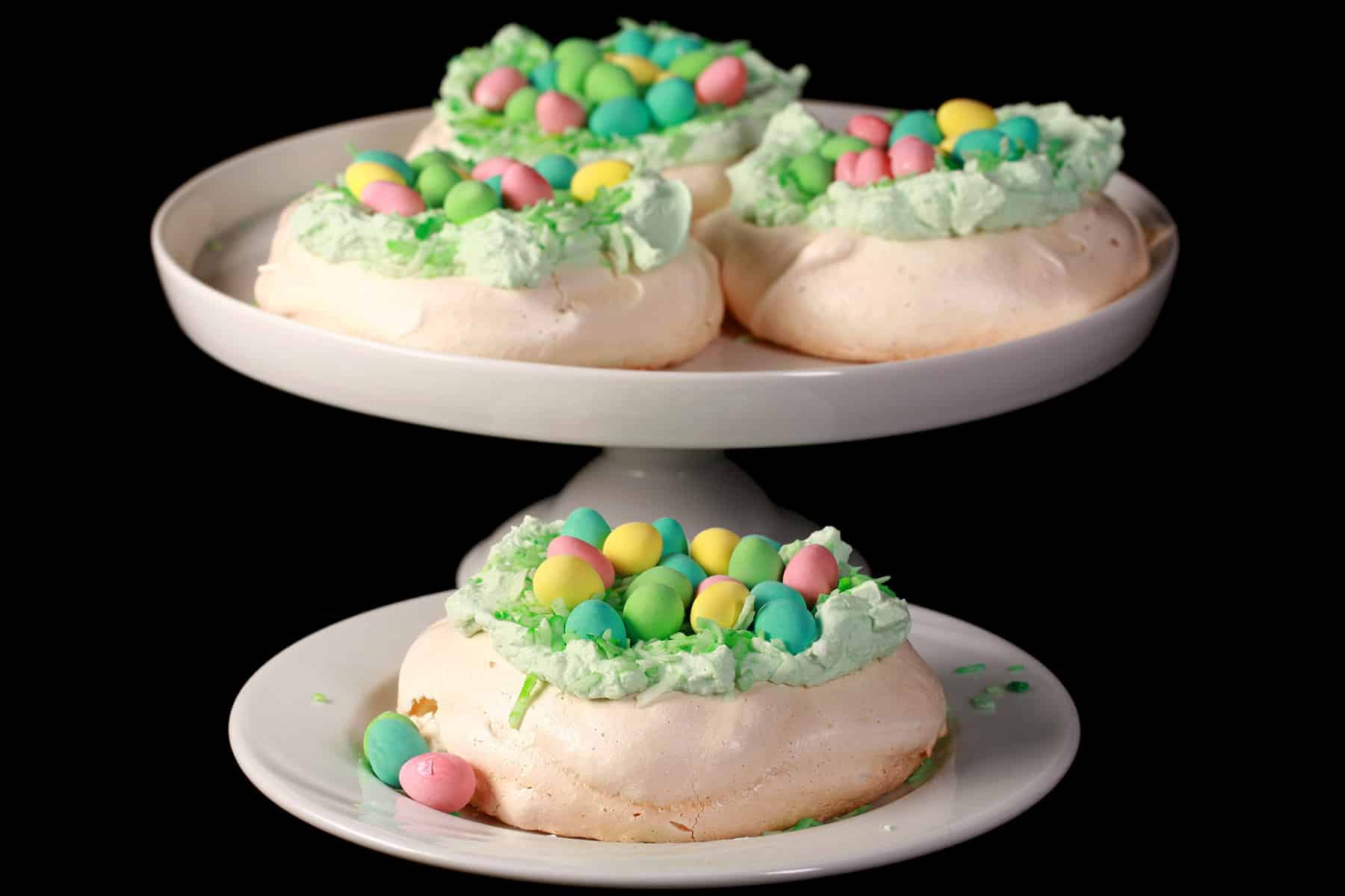 Mini easter pavlovas on a plate and a cake stand.  Each have green coconut and cadbury mini eggs on top.