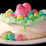 A single mini Easter pavlova, topped with green coconut and cadbury mini eggs and a pink Peeps marshmallow.