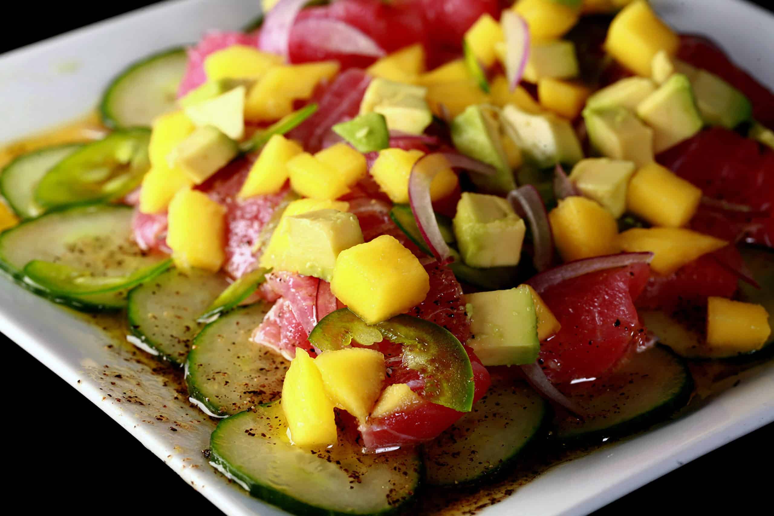 A close up photo of ahi tuna crudo, with mango, avocado, jalapenos, and a citrus vinaigrette, served over cucumber slices.