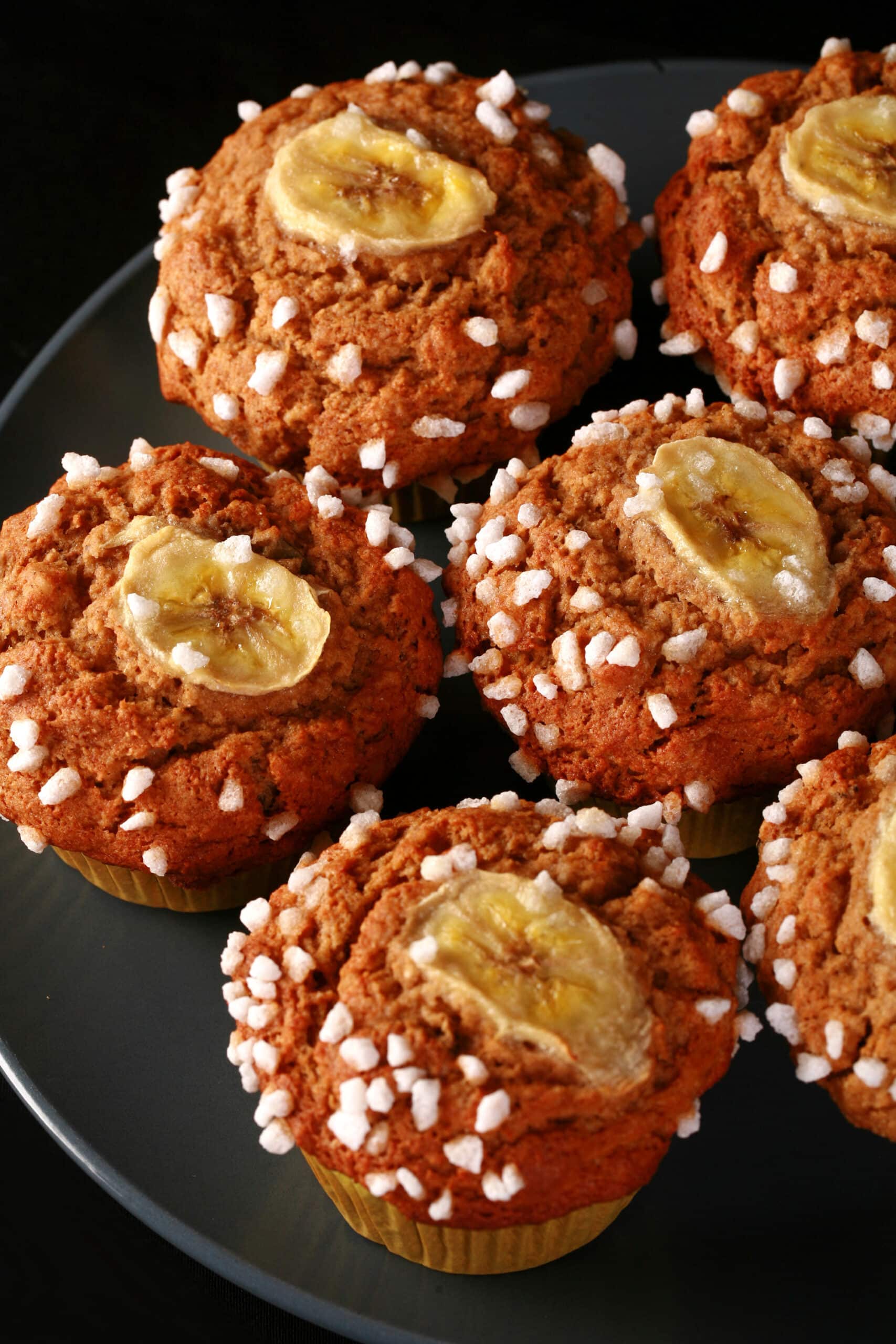 A plate of gluten free banana muffins, topped with coarse sugar and banana slices.