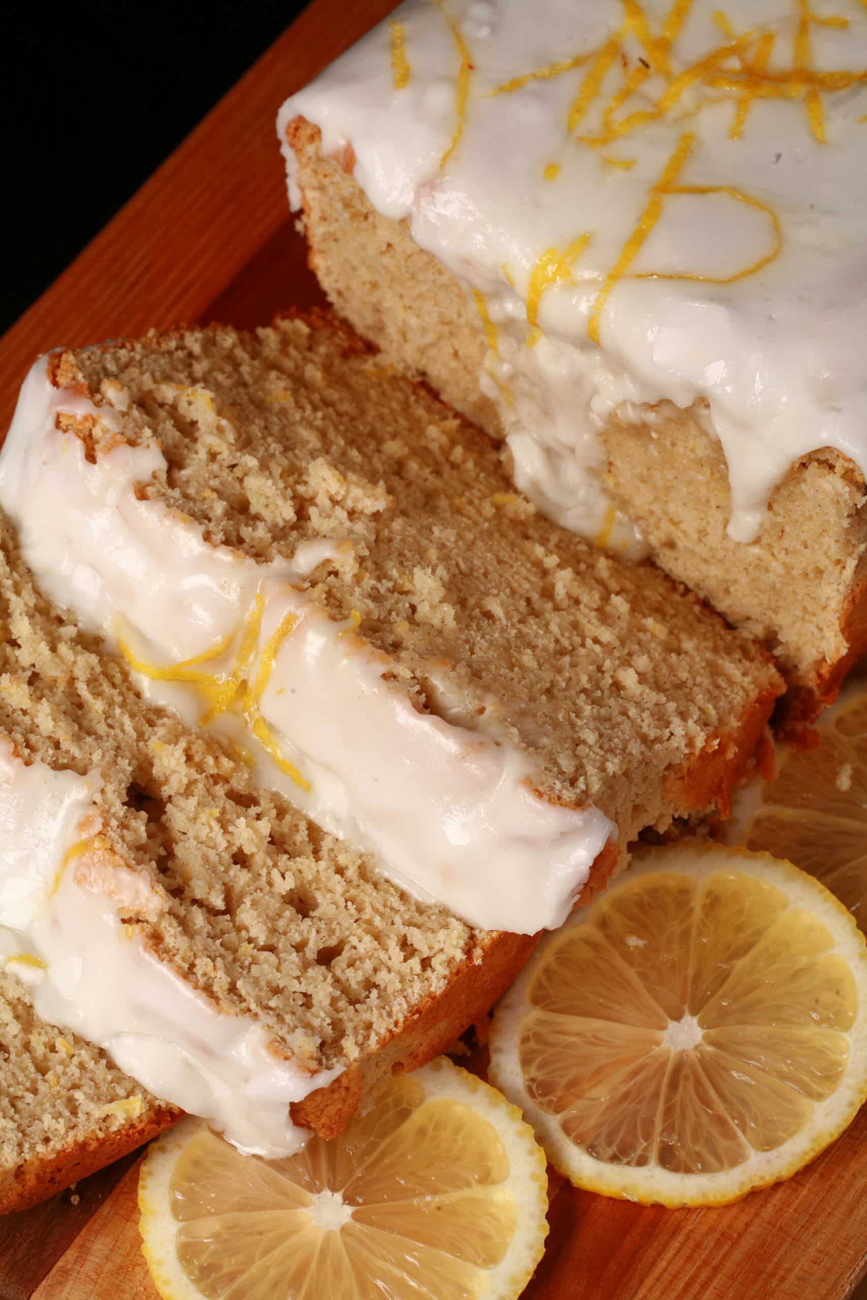 A sliced loaf of gluten-free lemon drizzle cake, with white glaze and lemon zest on top.