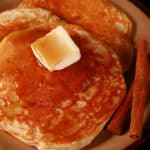 A close up view of 3 apple protein pancakes on a plate, topped with butter and maple syrup.