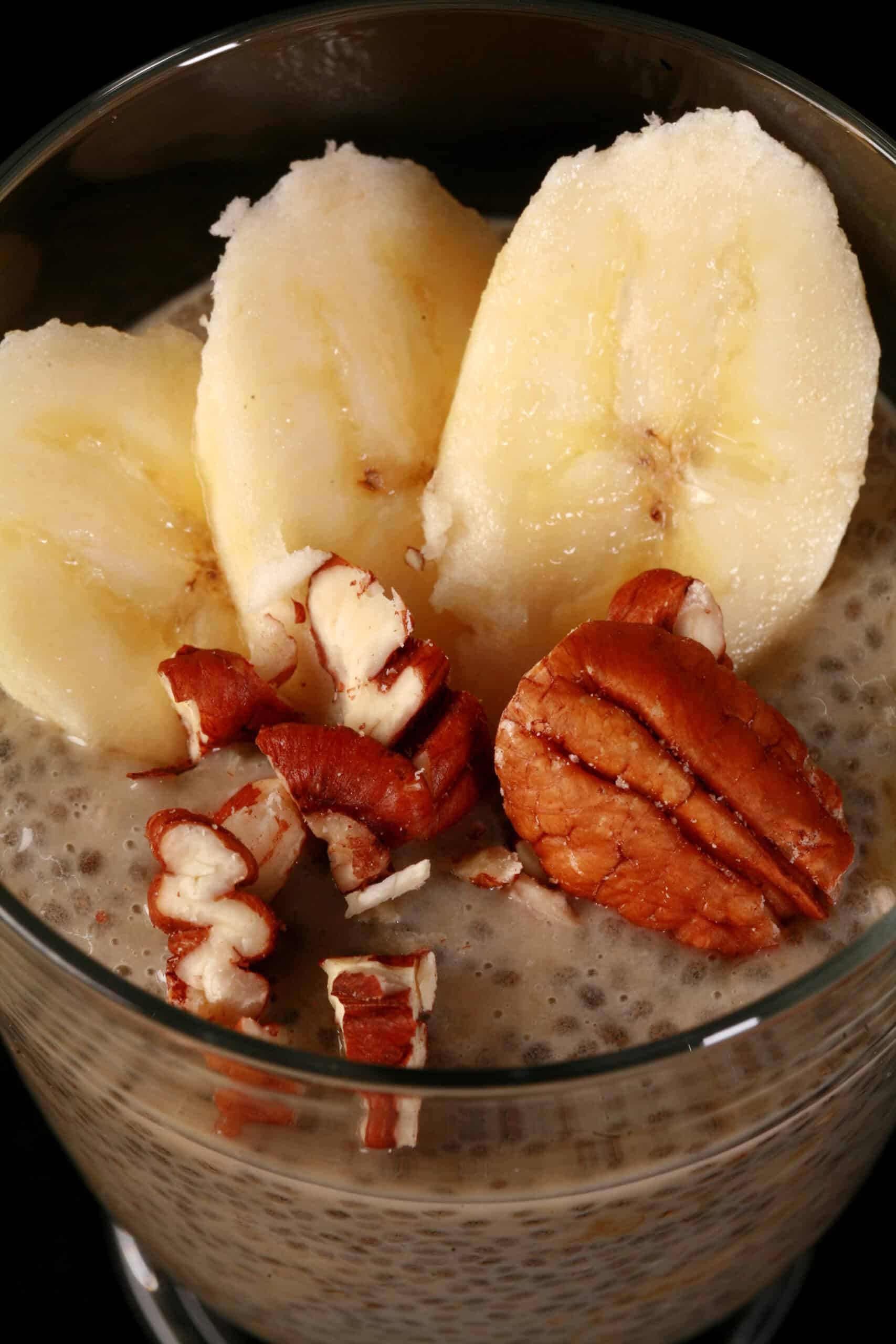 A close up view of a glass of banana chia pudding, topped with banana slices and pecans.