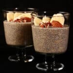 2 serving glasses of banana chia pudding, topped with banana slices and pecans.