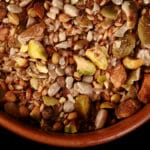 A small brown bowl of pistachio dukkag spice mix. Chunks of pistachios, coriander, sunflower seeds, and pumpkin seeds are visible.