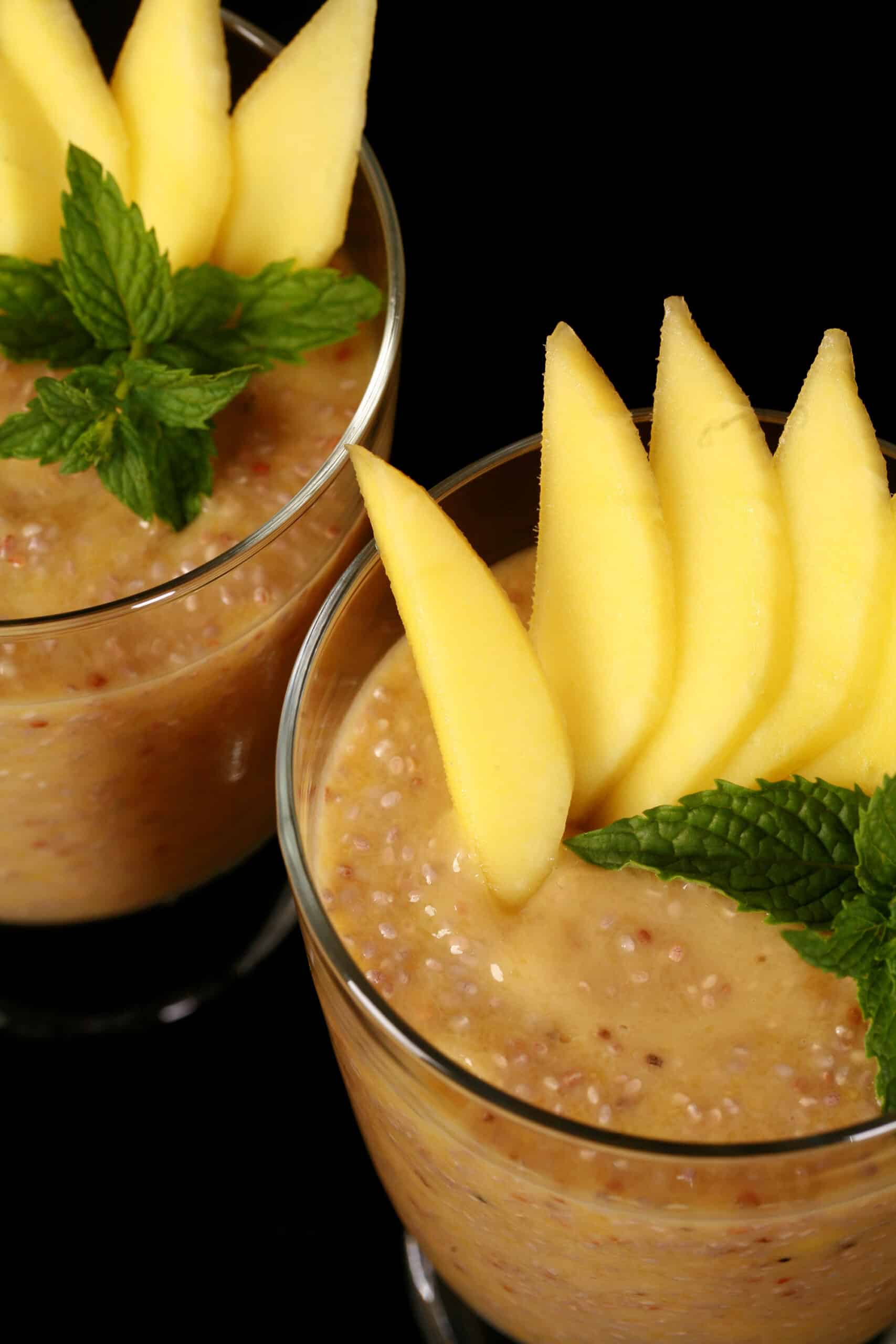 2 glasses of mango chia pudding, garnished with mango slices and fresh mint leaves.