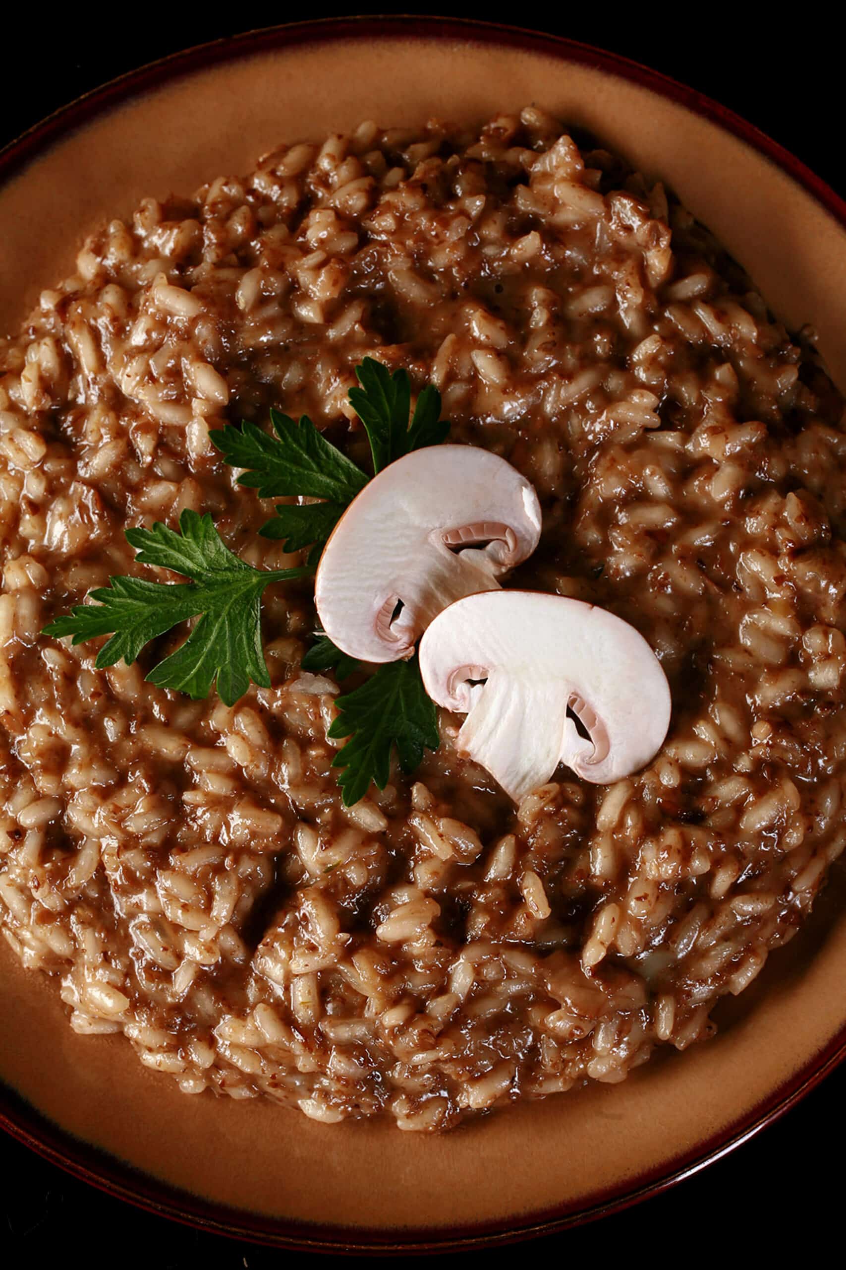 A plate of mushroom risotto, garnished with parsley leaves and sliced mushrooms.