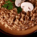 A plate of creamy mushroom risotto, garnished with parsley leaves and sliced mushrooms.