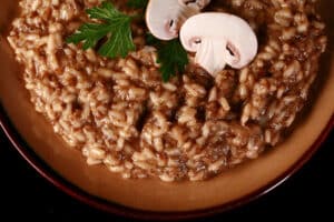 A plate of creamy mushroom risotto, garnished with parsley leaves and sliced mushrooms.