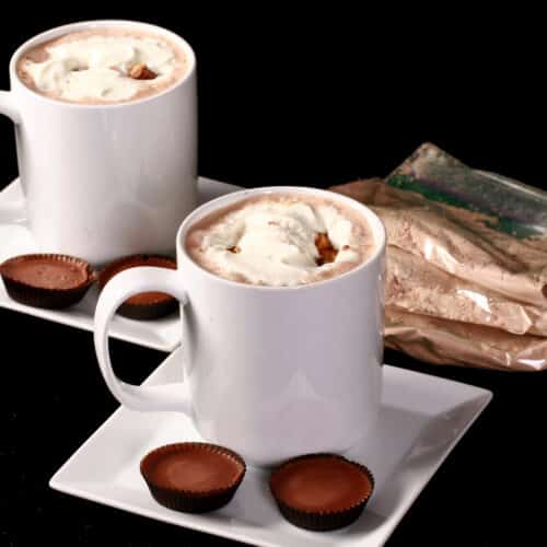 2 mugs of protein peanut butter cup hot chocolate with whipped cream and chopped peanut butter cups.