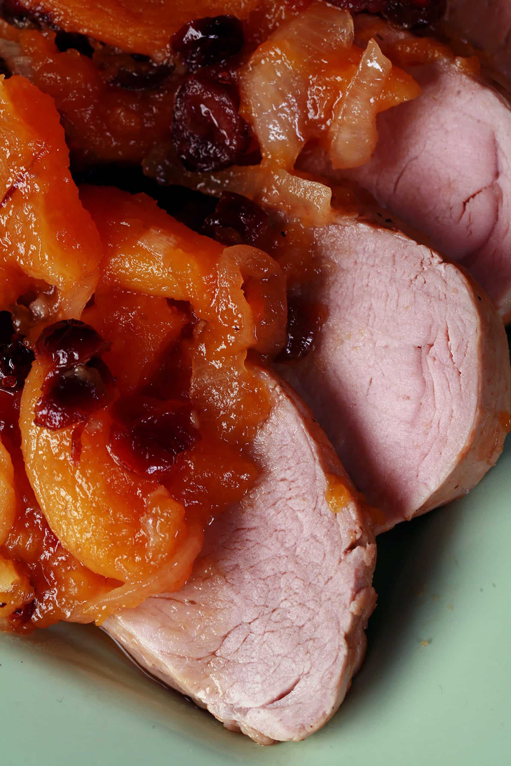 Slices of slow cooker pork tenderloin with stewed apricots and cranberries spooned over top.