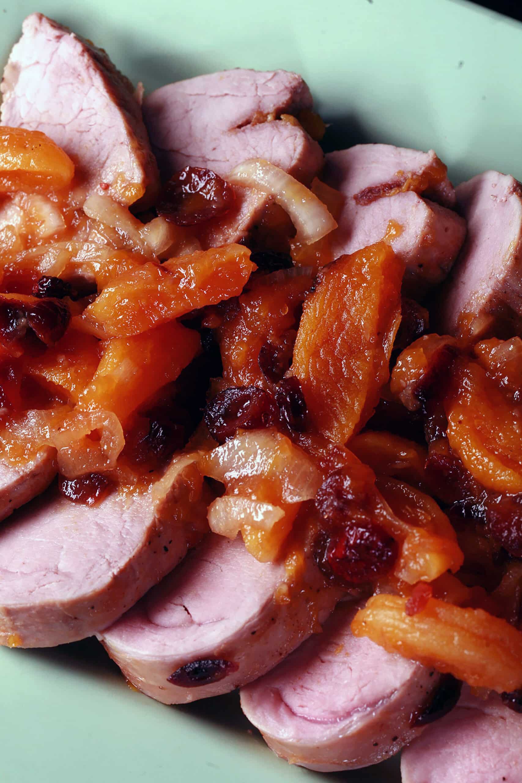 Slices of slow cooker pork tenderloin with stewed apricots and cranberries spooned over top.