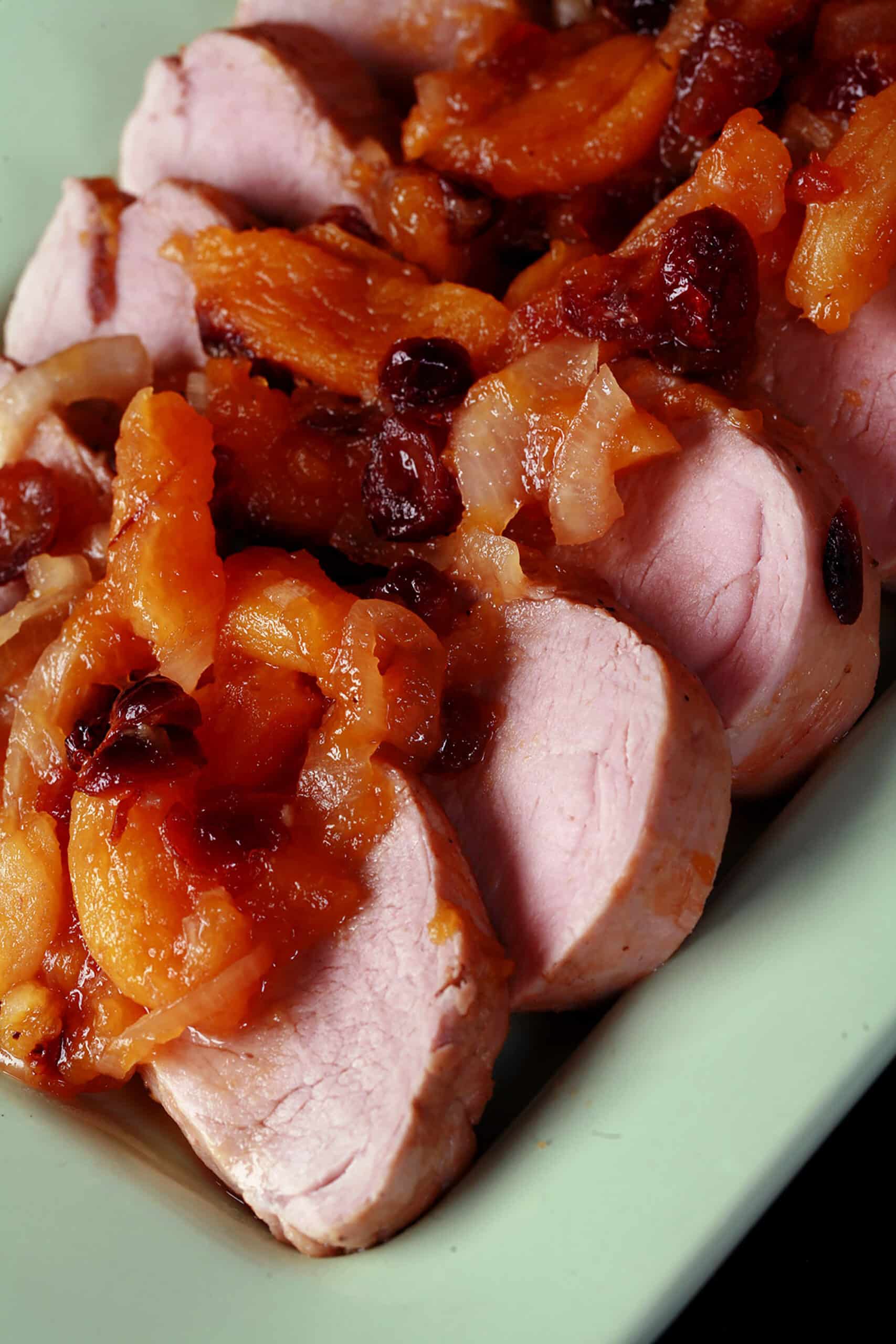 Slices of slow cooker pork tenderloin with stewed apricots and cranberries spooned over top.