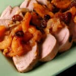 Slices of slow cooker pork tenderloin with stewed dried apricots and cranberries spooned over top.