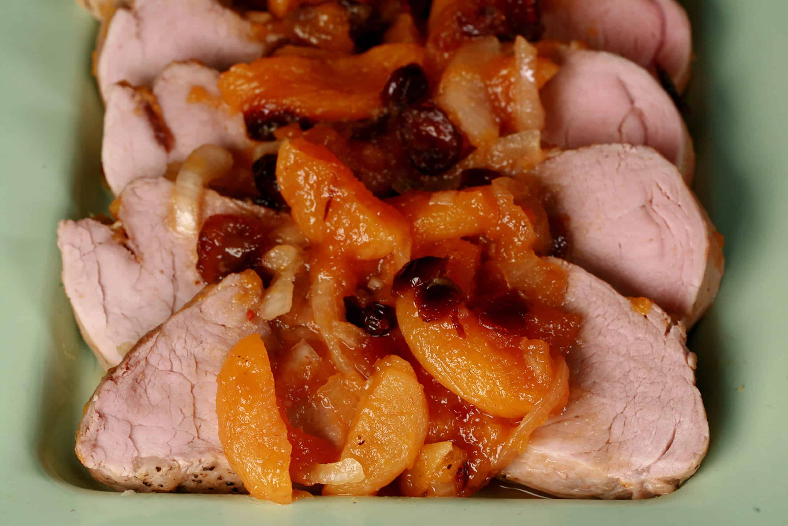 Slices of slow cooker pork tenderloin with stewed apricots and cranberries spooned over top.