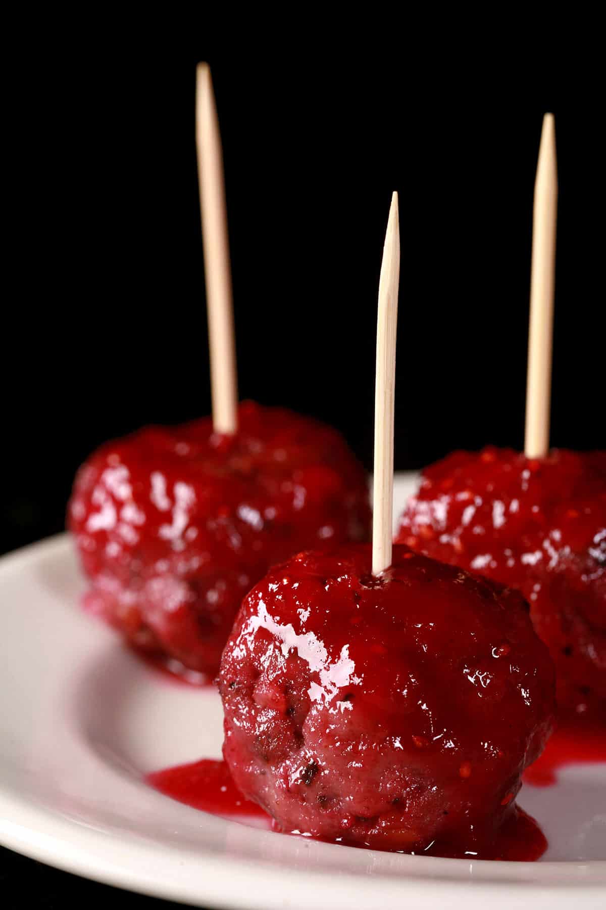 A close up photo of several gluten free turkey meatballs in cranberry glaze.  Each has a toothpick in it, and are arranged on a small plate.
