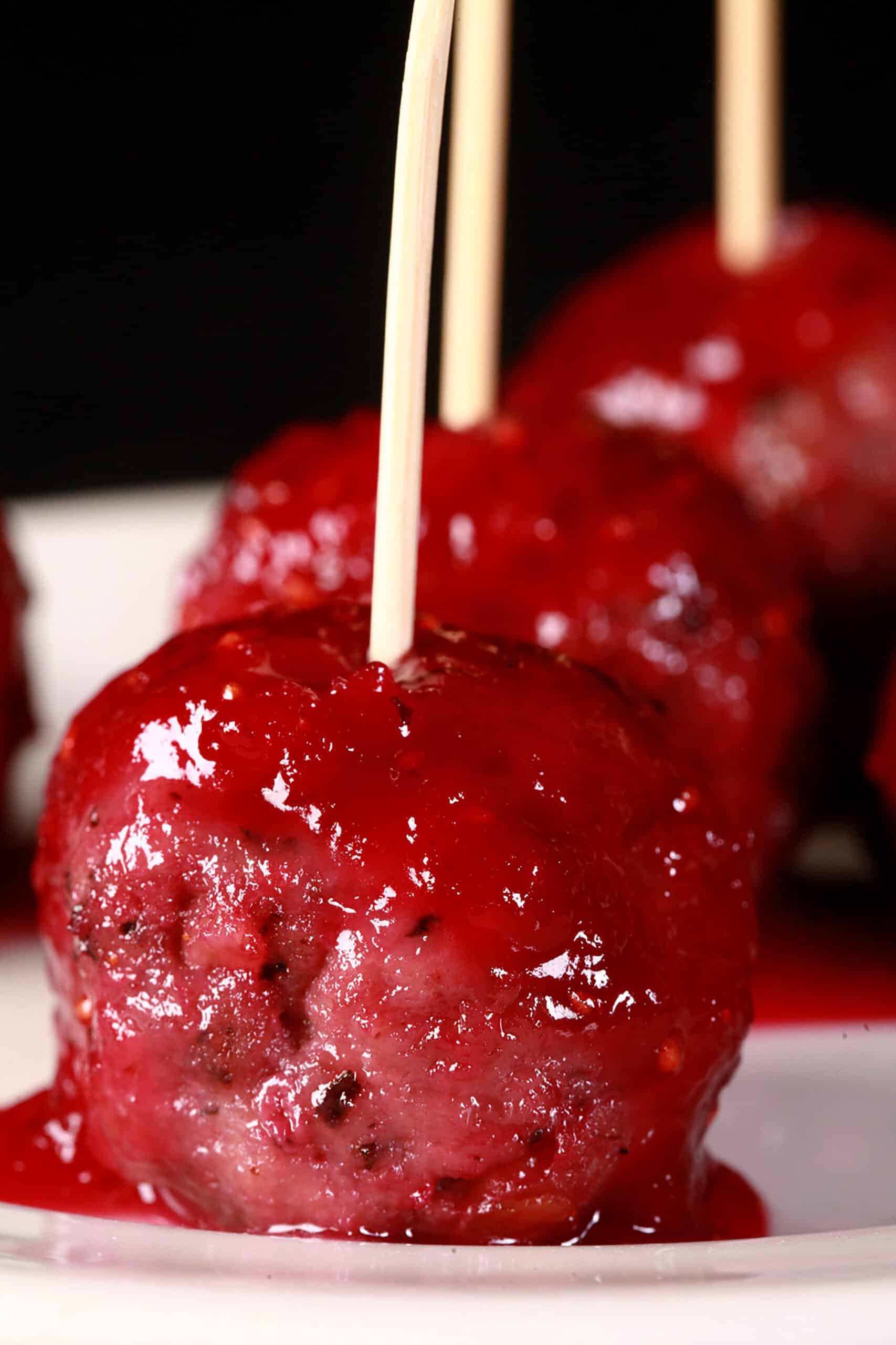 A close up photo of several gluten-free turkey meatballs in cranberry glaze.  Each has a toothpick in it, and are arranged on a small plate.