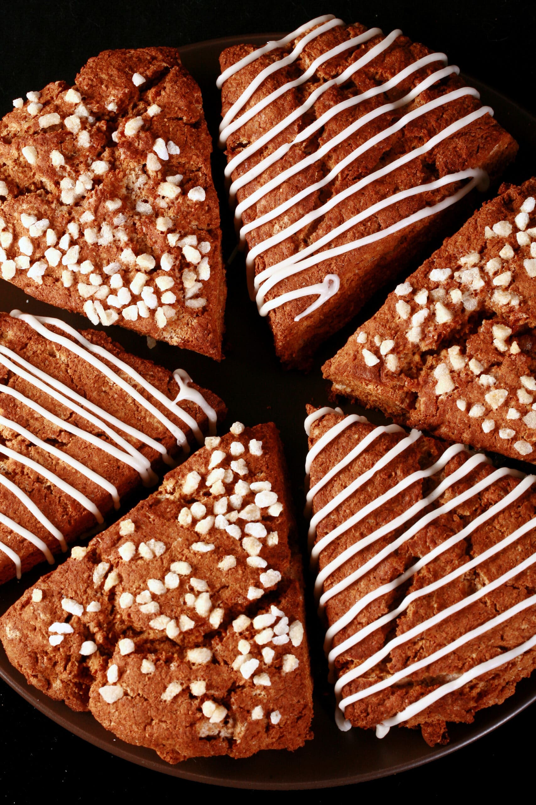 A plate of gluten-free gingerbread scones. Half have a sugar crust, the other half have a vanilla glaze drizzled over them.