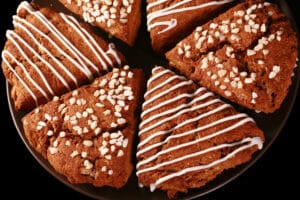 A plate of gluten-free gingerbread scones. Half have a sugar crust, the other half have a vanilla glaze drizzled over them.