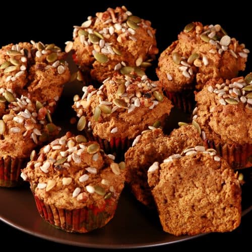 A plate of gluten-free pumpkin muffins, all topped with a mix of seeds and nuts.