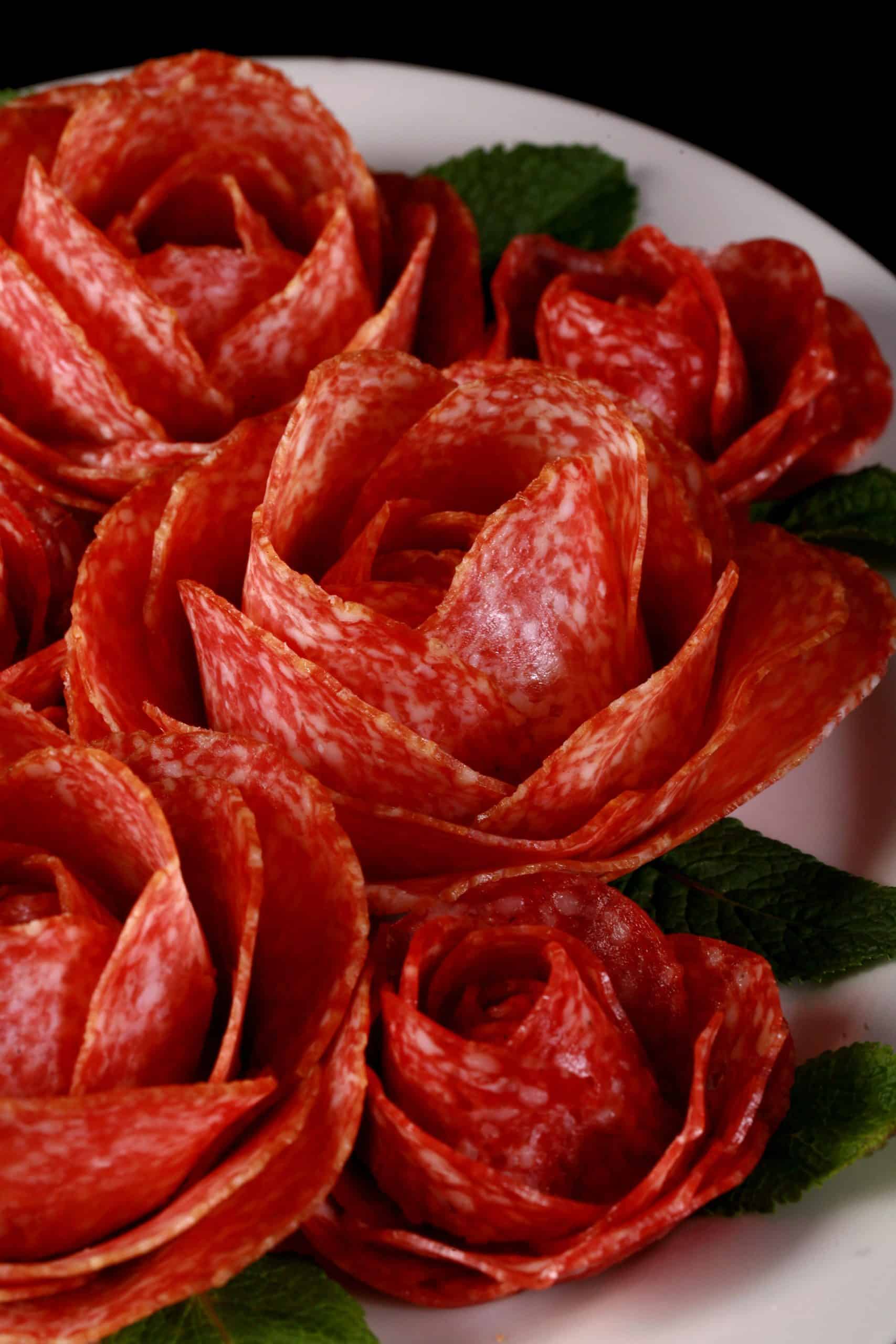 A plate of large and small salami roses, accented with mint leaves.