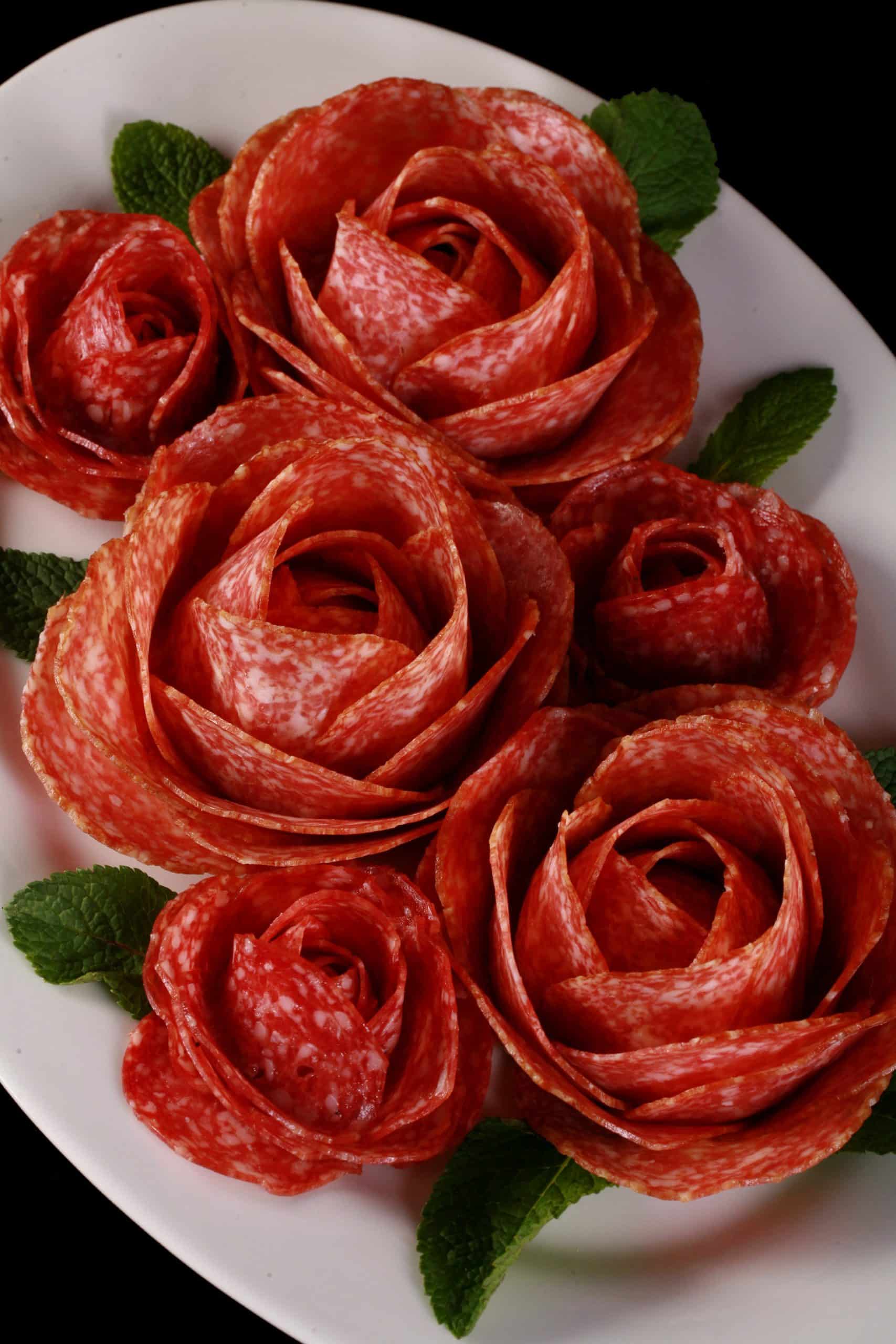 A plate of large and small charcuterie roses, accented with mint leaves.