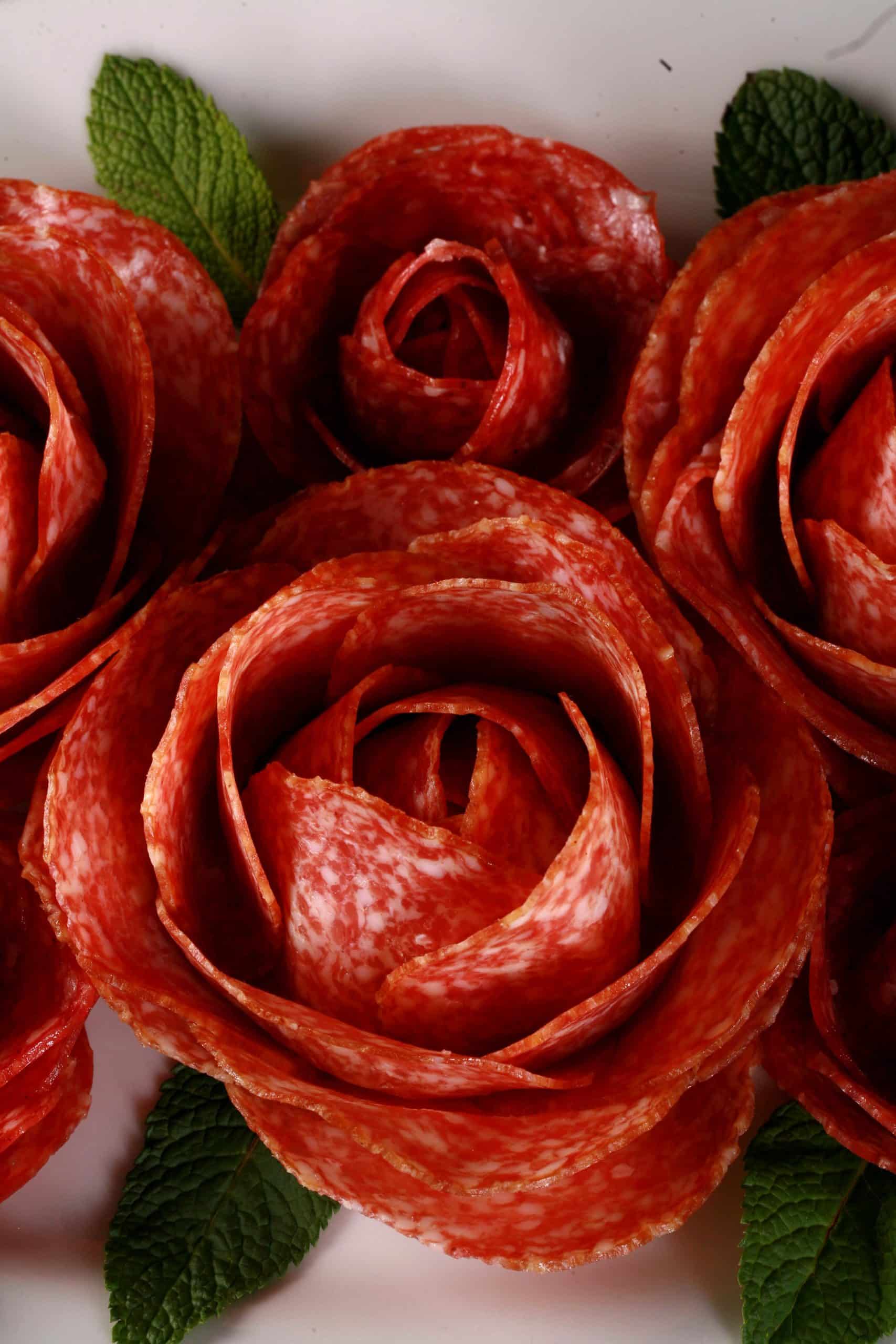 A plate of large and small salami roses, accented with mint leaves.