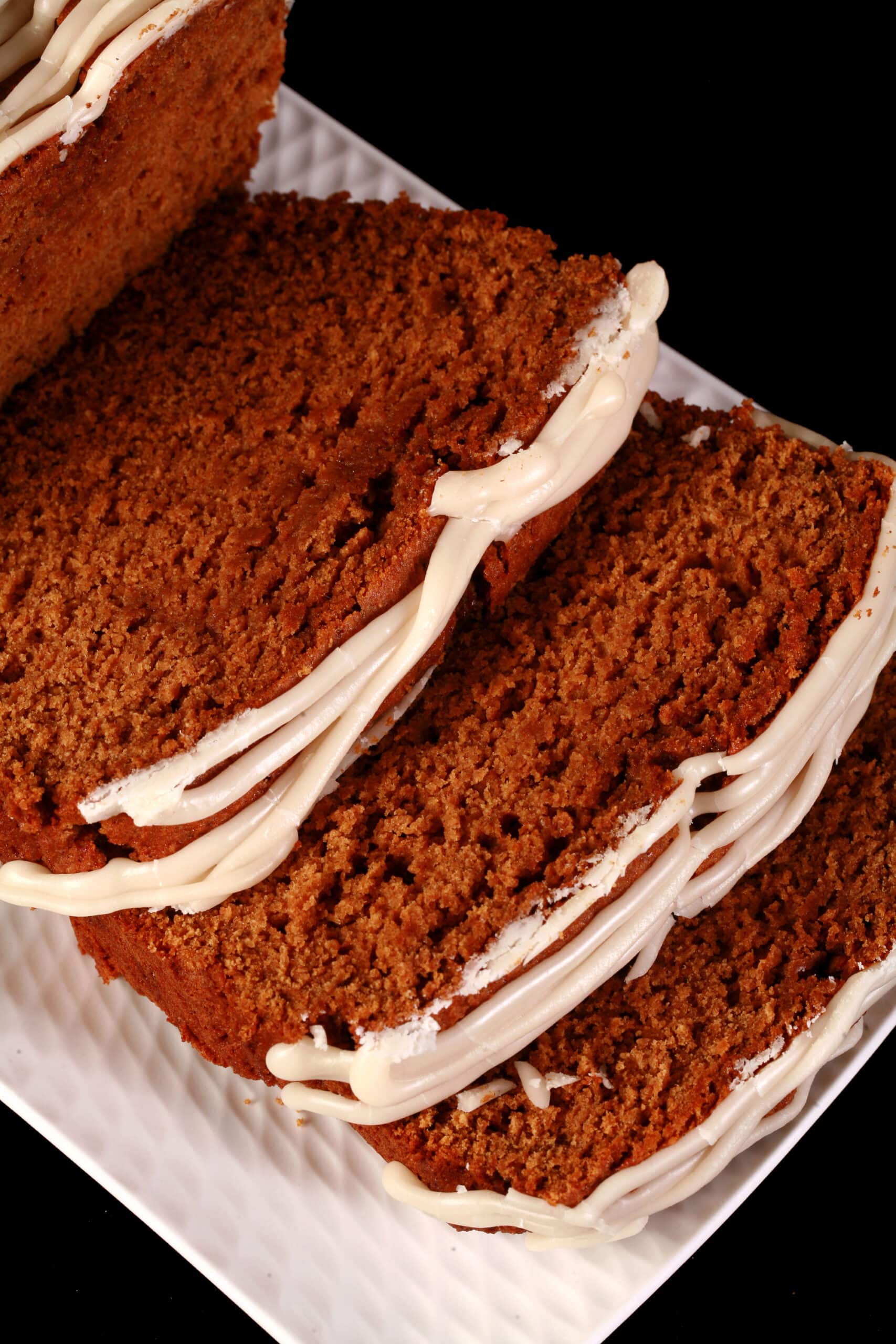 A sliced loaf of gluten-free gingerbread loaf, drizzled with vanilla glaze and garnished with rosemary and cranberries.