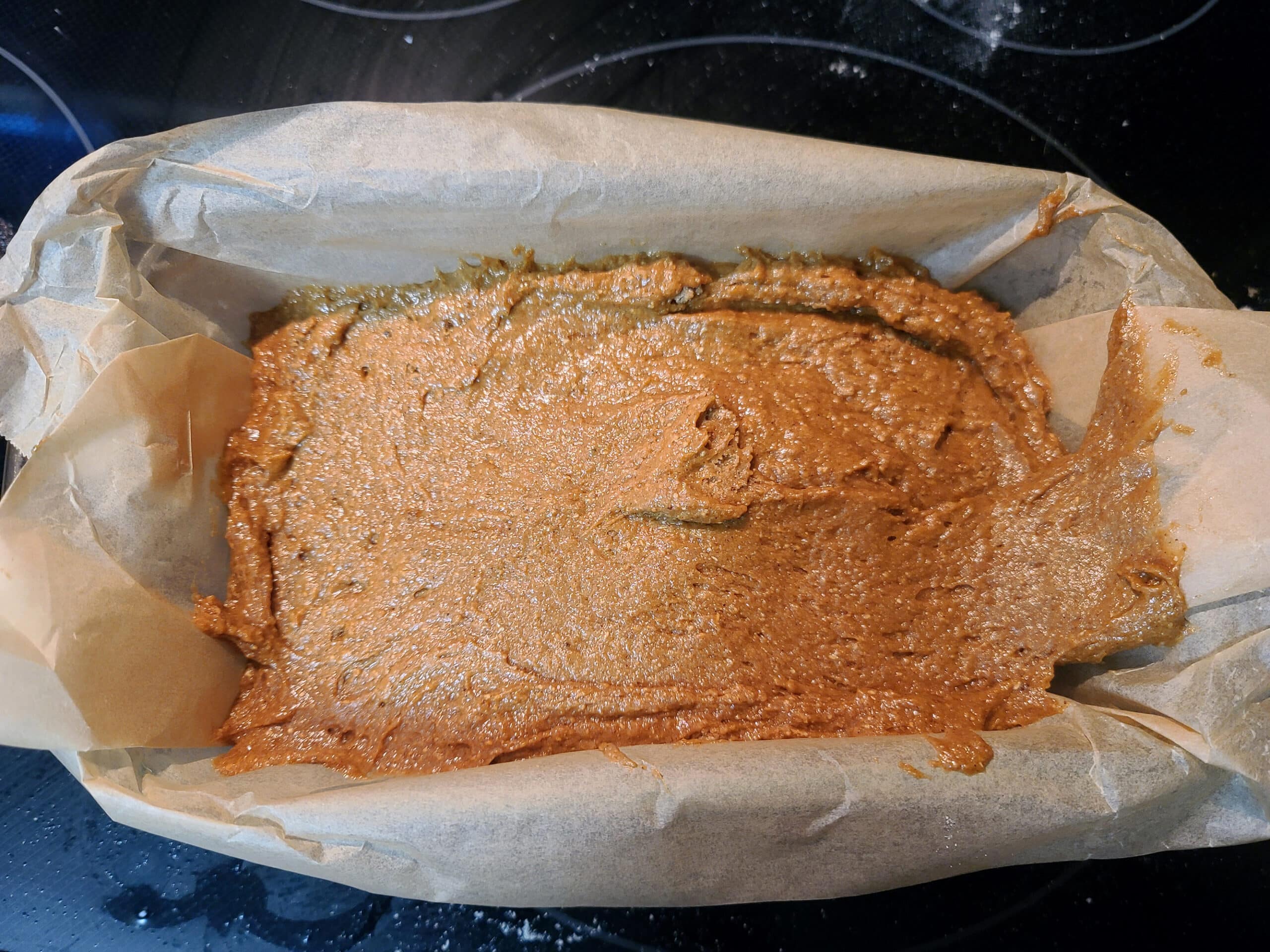 The gluten free gingerbread batter being spread in the prepared loaf pan.