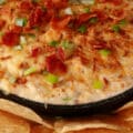 A cast iron pan of smoky hot bacon crab dip, surrounded by tortilla chips.