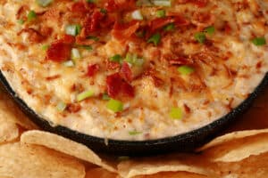 A cast iron pan of smoky hot bacon crab dip, surrounded by tortilla chips.