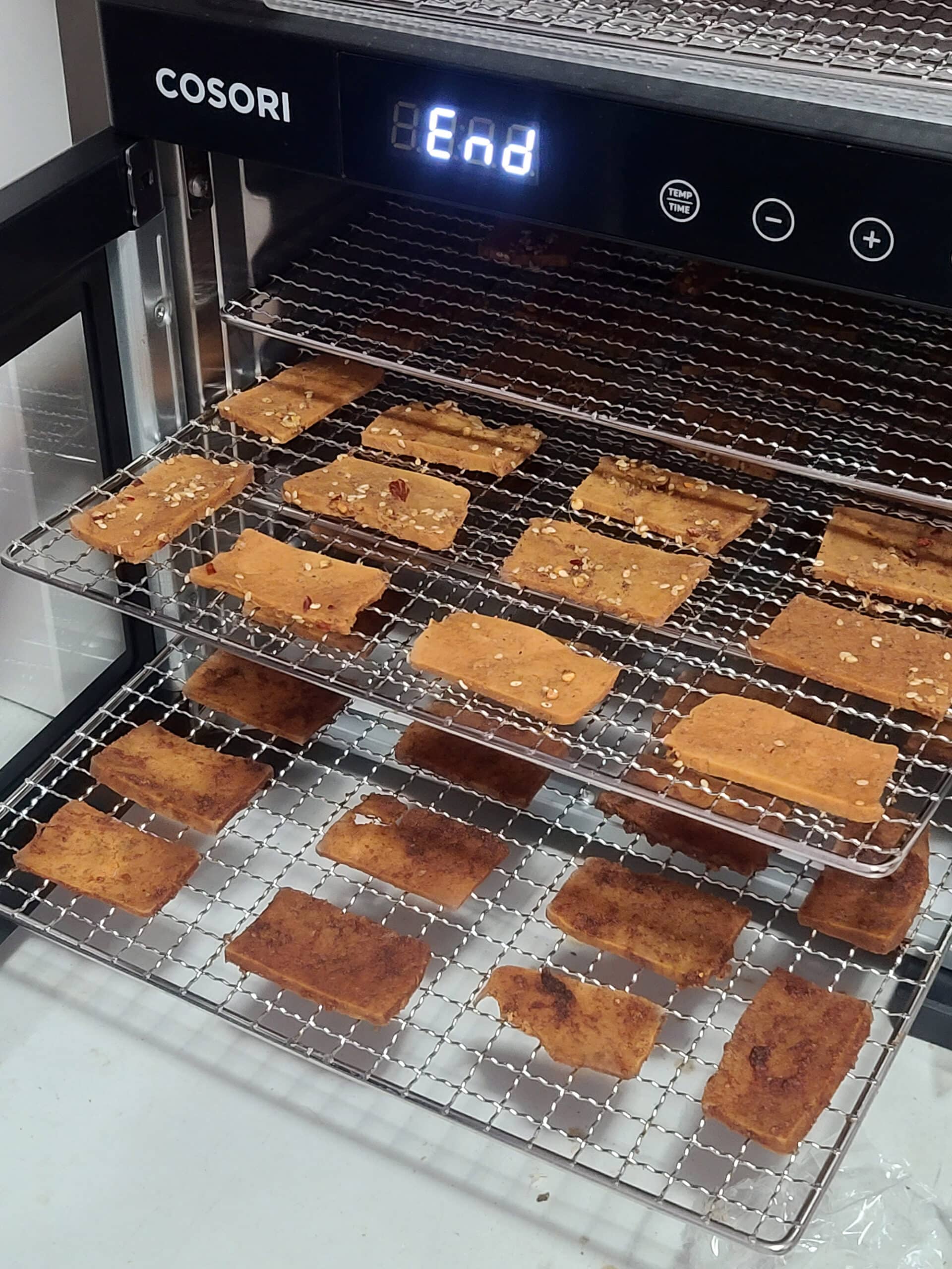 An open food dehydrator with trays of dehydrated tofu jerky pulled out.